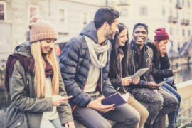 52899973 - multicultural group of friends using cellphones - students sitting in a row and typing on the smartphones